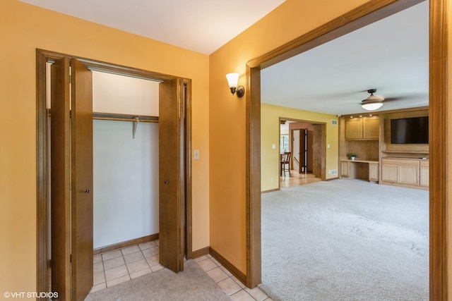 hall featuring baseboards, light tile patterned flooring, and light carpet