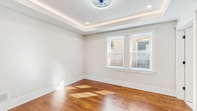 unfurnished bedroom featuring a tray ceiling, baseboards, visible vents, and wood finished floors