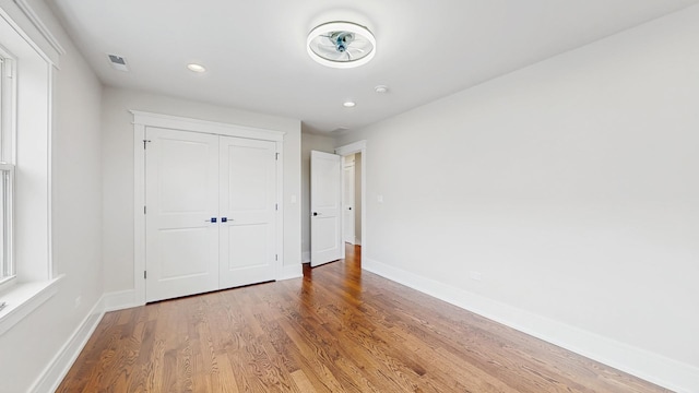 unfurnished bedroom with a closet, wood finished floors, baseboards, and recessed lighting
