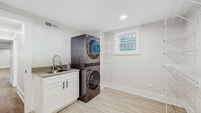 clothes washing area with stacked washer / dryer, a sink, cabinet space, visible vents, and baseboards