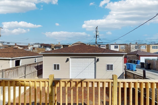 back of property featuring an outbuilding, roof with shingles, fence, and a detached garage