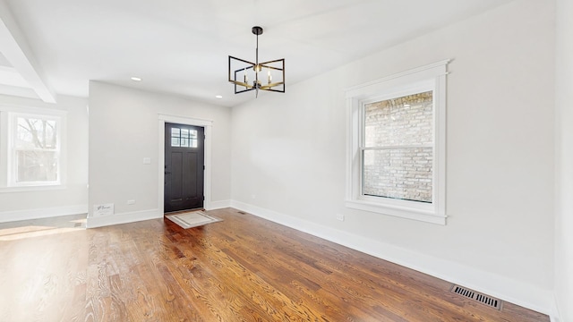 foyer entrance with an inviting chandelier, baseboards, visible vents, and wood finished floors