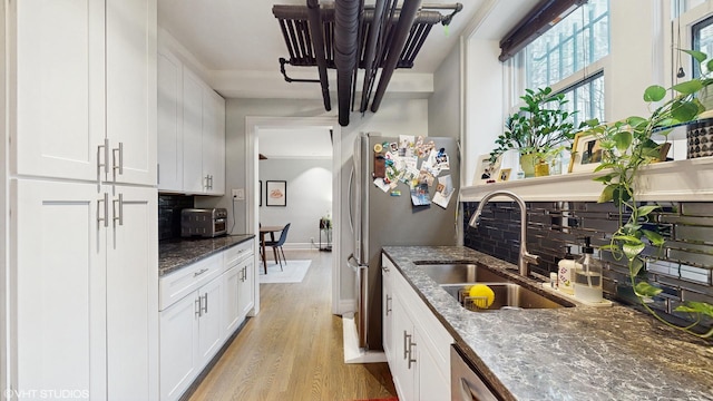 kitchen featuring a sink, tasteful backsplash, dark stone countertops, freestanding refrigerator, and light wood finished floors