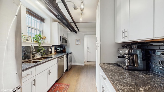 kitchen with a sink, dark stone countertops, backsplash, stainless steel appliances, and white cabinets