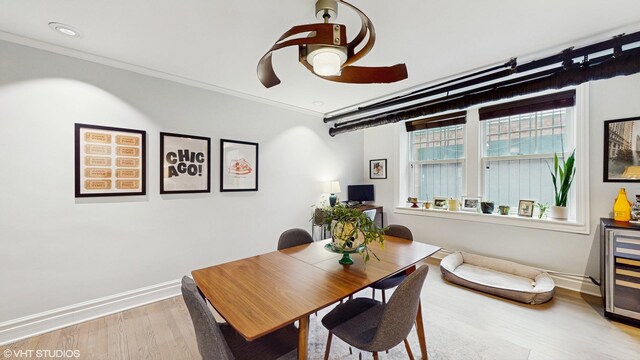 dining area featuring wine cooler, baseboards, ornamental molding, ceiling fan, and wood finished floors