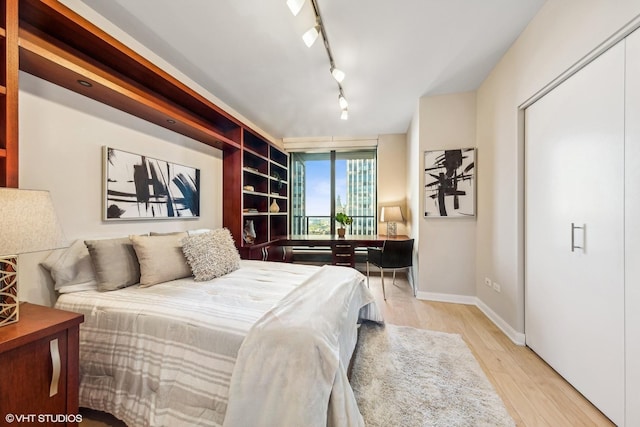 bedroom featuring baseboards, light wood-style floors, and rail lighting