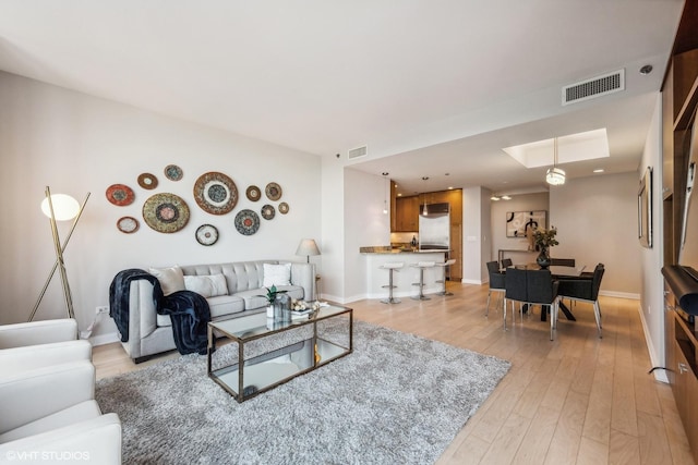 living room with light wood-type flooring, baseboards, and visible vents