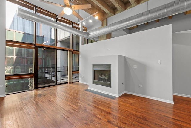 unfurnished living room with a high ceiling, a fireplace, wood finished floors, baseboards, and ceiling fan