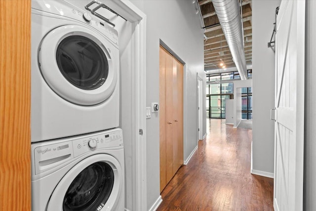 laundry room with stacked washer / drying machine, dark wood-style flooring, and baseboards