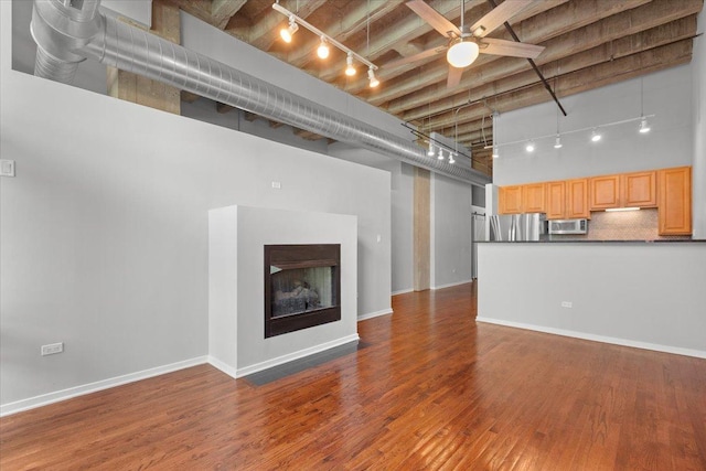 unfurnished living room featuring rail lighting, a towering ceiling, ceiling fan, wood finished floors, and a fireplace