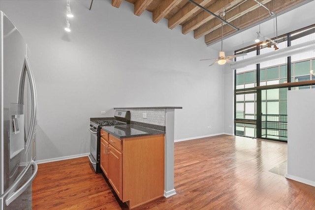 kitchen featuring appliances with stainless steel finishes, track lighting, a towering ceiling, a ceiling fan, and wood finished floors