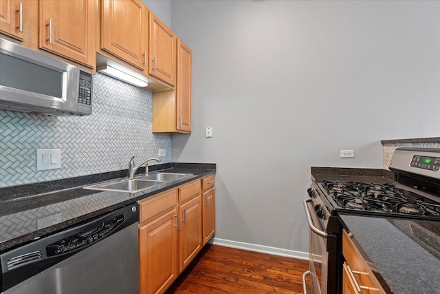 kitchen featuring stainless steel appliances, a sink, backsplash, dark wood finished floors, and baseboards