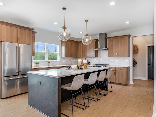kitchen featuring a kitchen island, high quality fridge, a sink, light wood-style floors, and wall chimney exhaust hood