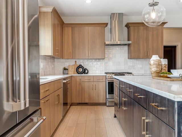 kitchen with wall chimney range hood, decorative backsplash, light stone countertops, light wood-style floors, and stainless steel appliances