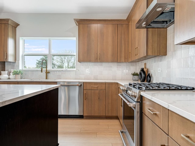 kitchen with backsplash, appliances with stainless steel finishes, light wood-type flooring, a sink, and extractor fan