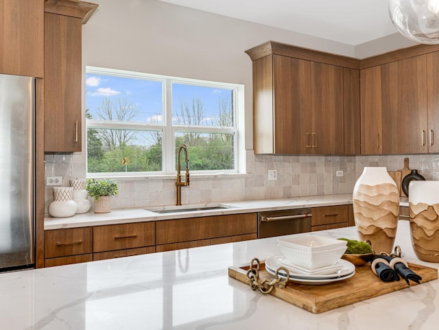 kitchen featuring a sink, appliances with stainless steel finishes, backsplash, and brown cabinets
