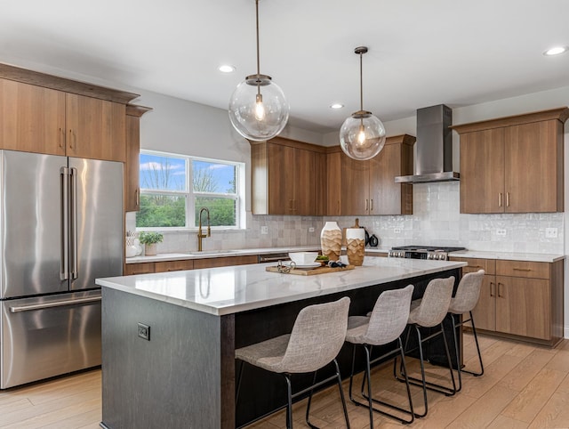 kitchen with wall chimney range hood, a sink, high end refrigerator, a center island, and light wood-type flooring