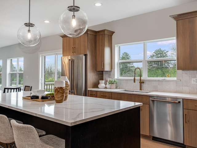 kitchen with brown cabinets, stainless steel appliances, light stone countertops, and a sink