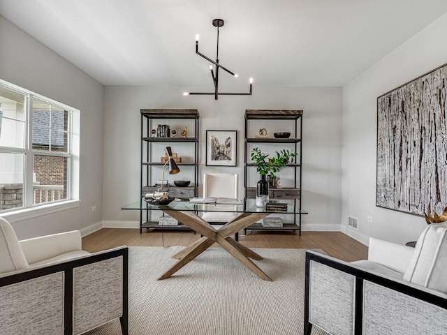 office space with baseboards, wood finished floors, visible vents, and an inviting chandelier