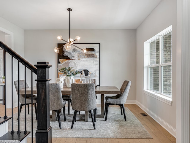 dining space with visible vents, light wood-type flooring, baseboards, an inviting chandelier, and stairs