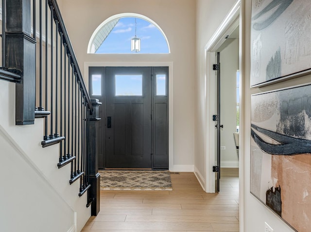 entryway featuring a towering ceiling, light wood finished floors, and stairs