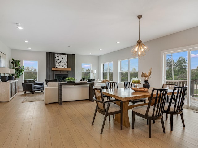 dining area featuring light wood-type flooring, an inviting chandelier, a wealth of natural light, and a large fireplace