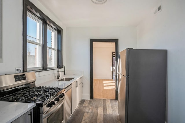 kitchen featuring appliances with stainless steel finishes, a sink, dark wood finished floors, and baseboards