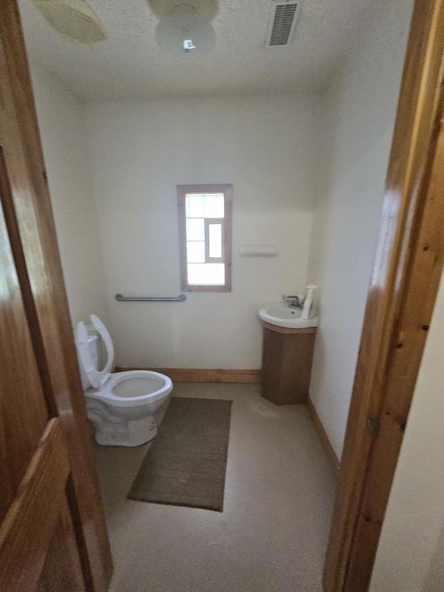 half bath featuring toilet, baseboards, visible vents, and a sink