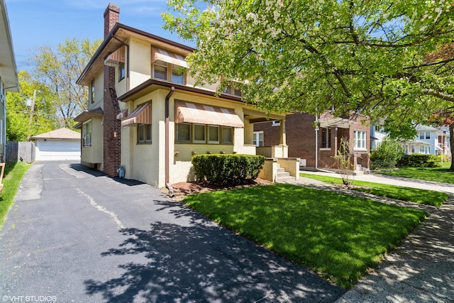 view of front of house featuring an outdoor structure, a chimney, a detached garage, stucco siding, and a front lawn