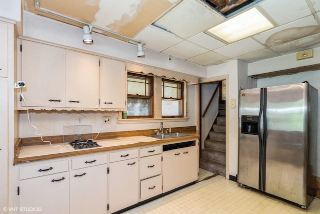 kitchen featuring stainless steel fridge, a sink, light floors, a drop ceiling, and white cabinets