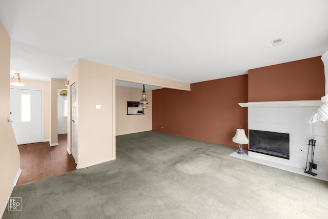 unfurnished living room with carpet floors and a tiled fireplace