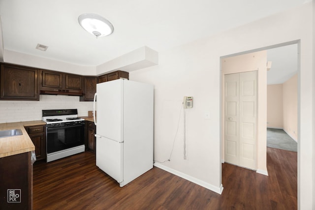kitchen featuring white appliances, under cabinet range hood, dark brown cabinetry, light countertops, and dark wood-style flooring