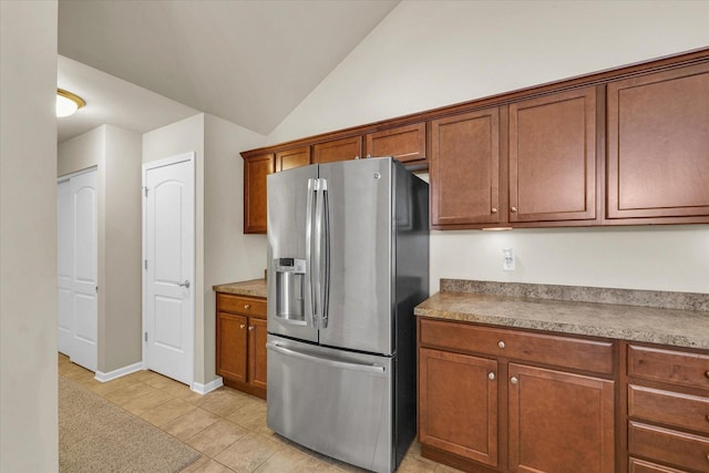 kitchen featuring stainless steel fridge, brown cabinets, light tile patterned floors, and vaulted ceiling