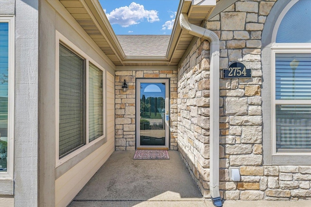 doorway to property featuring stone siding and roof with shingles