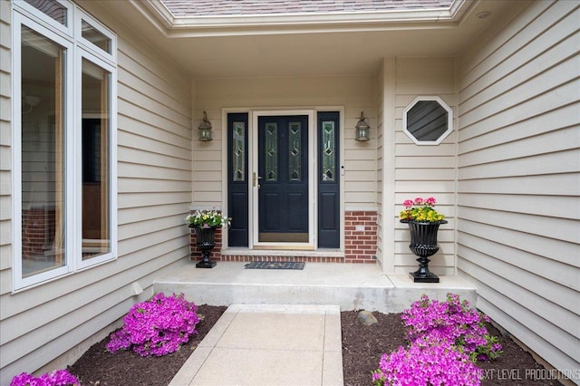 doorway to property with a shingled roof, a porch, and brick siding