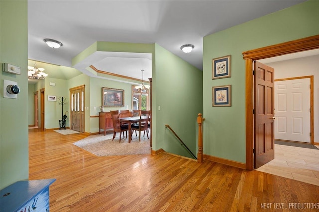 corridor with a chandelier, an upstairs landing, light wood-style floors, and baseboards