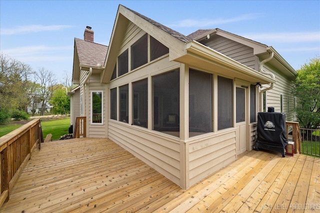 view of home's exterior with a wooden deck, a chimney, a sunroom, and roof with shingles