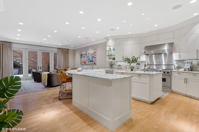 1442 W Cuyler Ave, Chicago, IL 60613 - kitchen featuring crown molding, a center island with sink, light wood-style flooring, and wall chimney exhaust hood