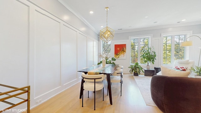 dining area featuring light wood finished floors, a decorative wall, and crown molding