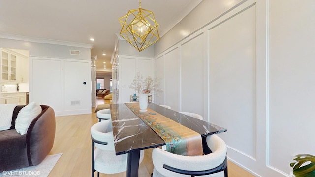 dining space featuring a chandelier, light wood-style flooring, recessed lighting, a decorative wall, and ornamental molding