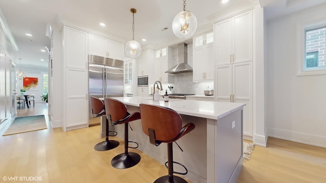 kitchen featuring built in appliances, wall chimney exhaust hood, light wood-style floors, backsplash, and a sink