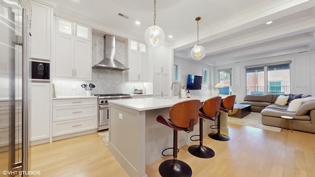 kitchen with wall chimney exhaust hood, high end range, a sink, light wood finished floors, and open floor plan