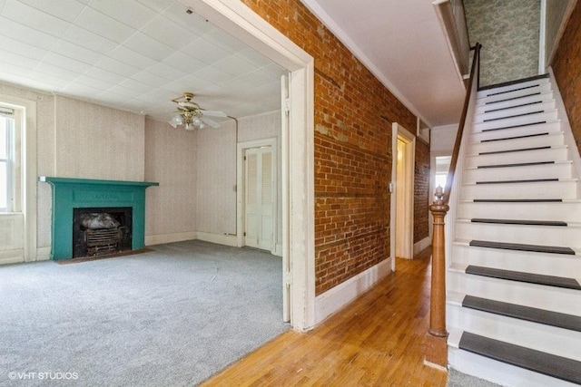 1027 Paul St, Ottawa, IL 61350 - unfurnished living room with ceiling fan, brick wall, a fireplace with flush hearth, stairway, and light wood finished floors
