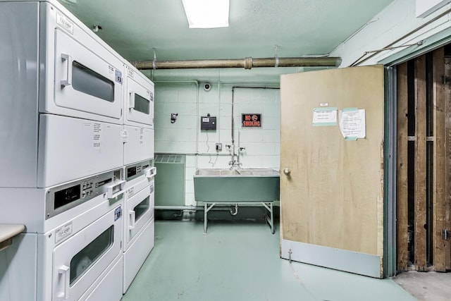 below grade area with stacked washer and clothes dryer and a sink