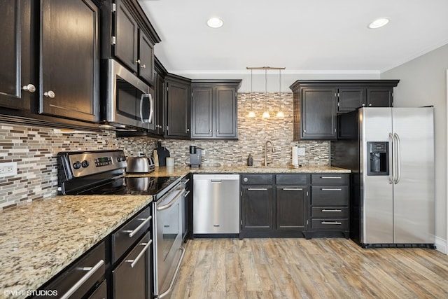 kitchen with appliances with stainless steel finishes, a sink, light wood finished floors, light stone counters, and ornamental molding