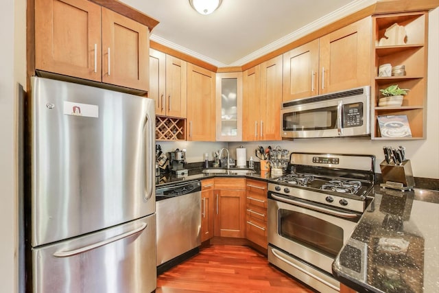 kitchen with appliances with stainless steel finishes, a sink, dark stone countertops, glass insert cabinets, and dark wood-style floors