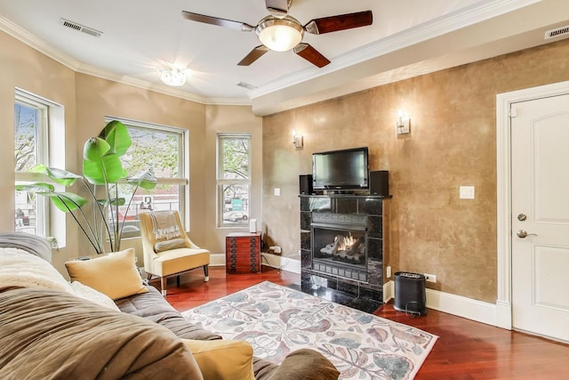 living area featuring wood finished floors, baseboards, ornamental molding, a ceiling fan, and a tile fireplace