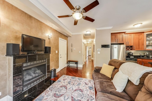 living room with ceiling fan, crown molding, a tile fireplace, and baseboards