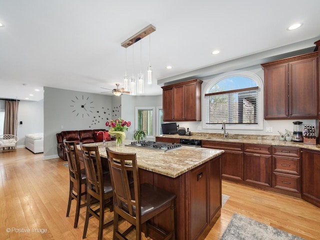 kitchen featuring stainless steel gas cooktop, a sink, open floor plan, a kitchen island, and light wood-style floors