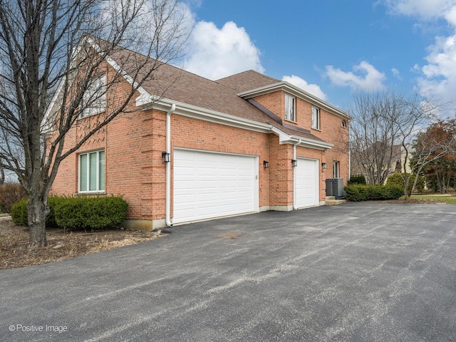view of side of home with central air condition unit, a shingled roof, brick siding, and driveway